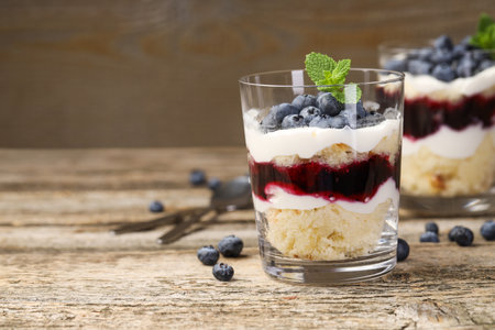 Trifle dessert with sponge cake, blueberries, jam and whipped cream in glasses on wooden table, closeupの写真素材
