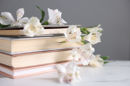 Books and beautiful alstroemeria flowers on white marble table against gray background, closeupの写真素材
