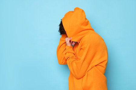 Person in orange hoodie against light blue background. Space for textの写真素材
