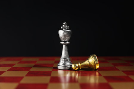 Silver king and fallen golden pawn on chessboard against black background, closeup. Competition...