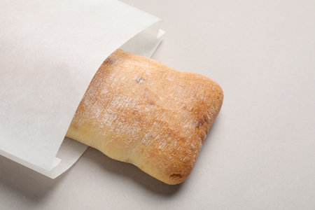 Paper bag with fresh ciabatta on beige background, closeup. Space for textの写真素材