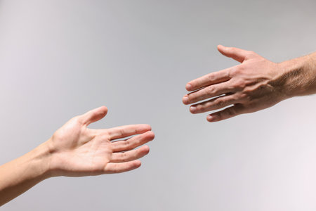 Two hands reaching toward each other on light gray background, closeupの写真素材