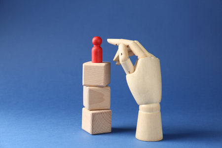 Competition concept. Human figure on wooden cubes and hand model against blue backgroundの写真素材