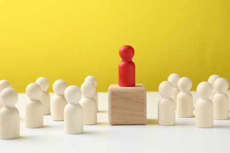Human figures around wooden block with red figure on top against yellow background. Competition conceptの写真素材