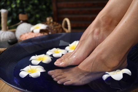 Feet soaking in bowl with water and plumeria flowers on floor, closeup. Spa treatmentの写真素材