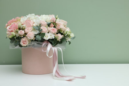 Gift box with bouquet of beautiful flowers and eucalyptus branches on white table against green...