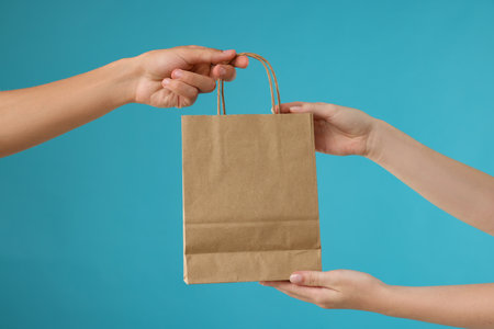 Person giving customer's order in paper bag on light blue background, closeupの写真素材