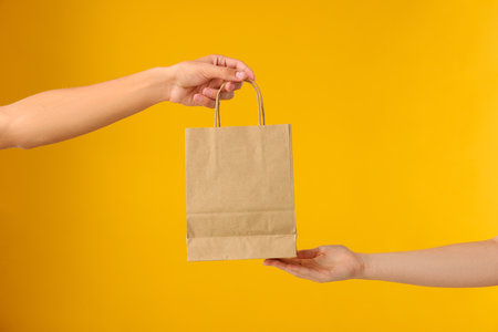 Person handing over a paper bag against orange background, closeupの写真素材