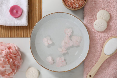 Bowl of water with flowers and different spa supplies on white marble table, flat layの写真素材