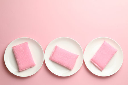 Sponges and plates on pink background, flat lay