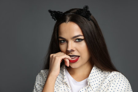 Portrait with cat-themed makeup and ears against grey backgroundの写真素材