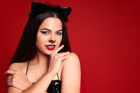 Portrait with cat-themed makeup and ears against a red backgroundの写真素材