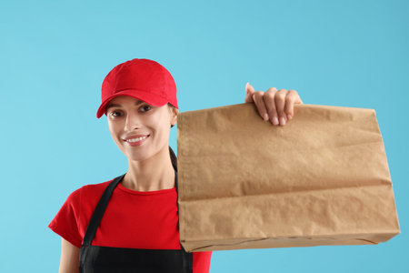 Fast-food worker with paper bag on light blue backgroundの写真素材