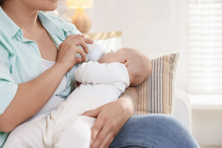 Mother feeding her cute baby indoors, closeup