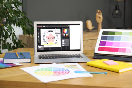 Designer's workplace with laptop, tablet, stationery and palettes on wooden table indoors
