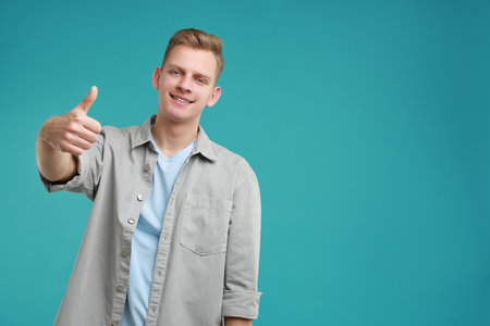 Person showing thumbs up on turquoise background, space for text. Like gestureの写真素材