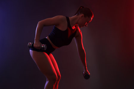 Woman exercising with dumbbells in smoke on dark backgroundの写真素材