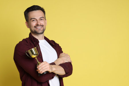 Happy winner with golden trophy cup on yellow background, space for textの写真素材