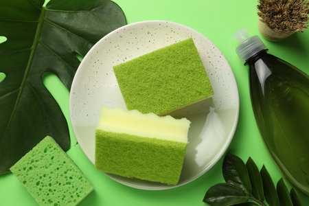 Flat lay composition with sponges, brush and detergent on green backgroundの写真素材