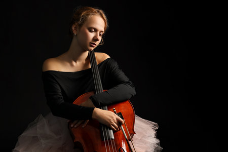 Beautiful young woman with cello on black background
