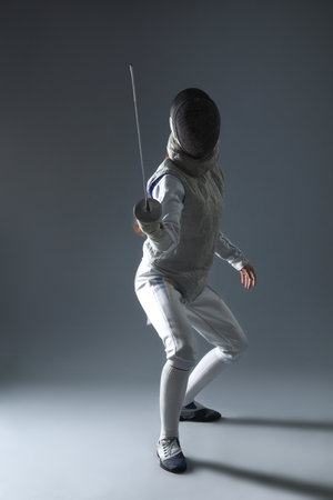 Fencer with epee practicing on gray background