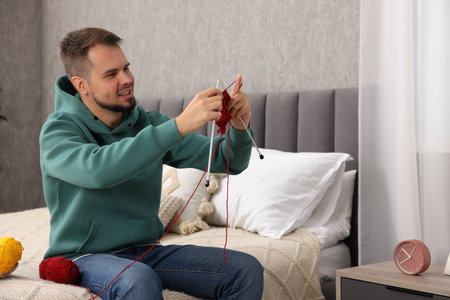 Man knitting with needles on bed at homeの写真素材