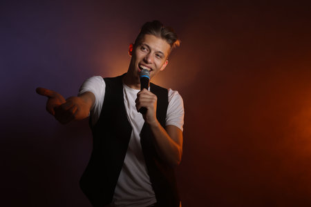 Talented young man singing on dark background with color lightの写真素材