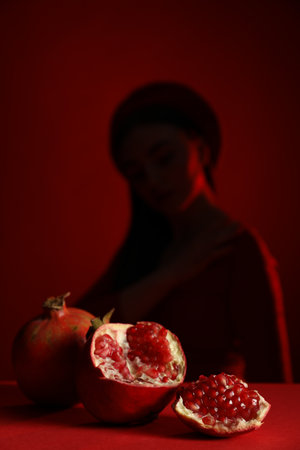 Woman posing against dark red background, focus on ripe pomegranateの写真素材