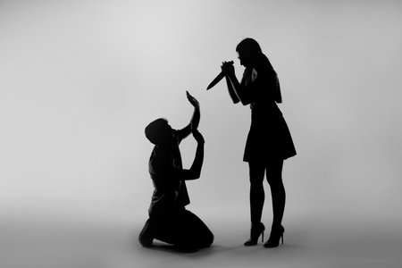 Domestic violence. Silhouette of woman with knife threatening her husband on grey backgroundの写真素材