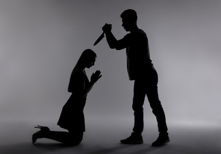 Domestic violence. Silhouette of man with knife threatening his wife on grey backgroundの写真素材