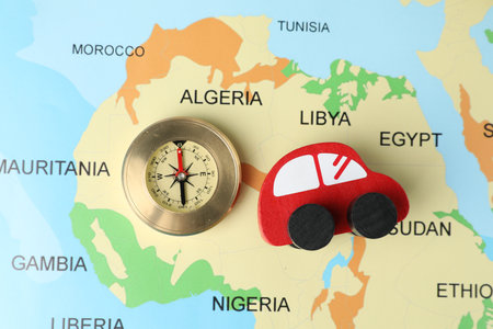 Red wooden toy car and compass on world map, top view. Road trip