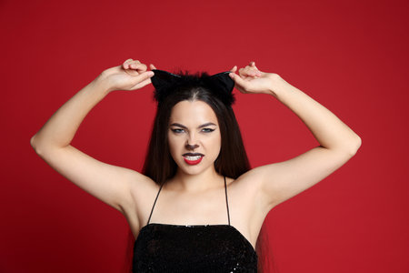 Beautiful woman with cat makeup and ears on red backgroundの写真素材