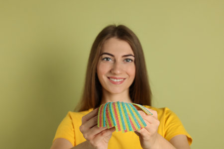 Happy young woman with tasty rainbow sour belts on olive background, selective focusの写真素材