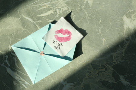 Note with phrase Kiss Me, lipstick mark and envelope on gray marble table, top view. Space for textの写真素材