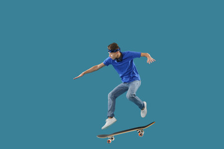 Handsome man with skateboard in air on blue background. Performing trickの写真素材