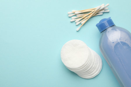 Clean cotton pads, swabs and micellar water on light blue background, flat lay. Space for textの写真素材