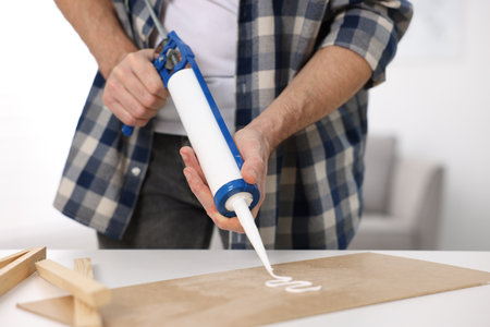 Man with caulking gun glueing plywood at white table indoors, closeupの写真素材