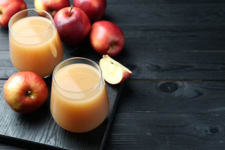 Refreshing apple juice in glasses and fruits on black wooden table, closeup. Space for textの写真素材