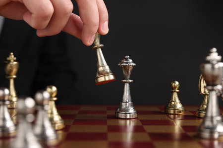 Businessman playing chess on chessboard against black background, closeup. Competition conceptの写真素材