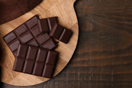 Pieces of delicious dark chocolate bar on wooden table, top view. Space for textの写真素材