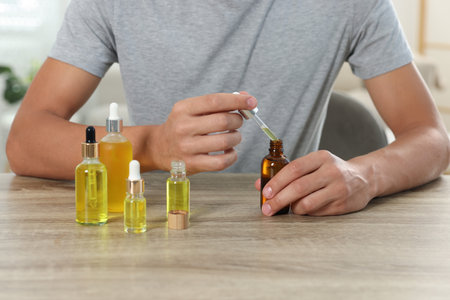 Young man dripping CBD tincture into bottle from dropper at wooden table, closeupの写真素材