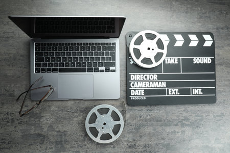 Movie clapper, film reels and laptop on grey textured table, flat layの写真素材