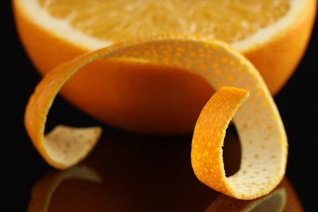 One curly orange peel and half of fruit on black mirror surface, closeupの写真素材