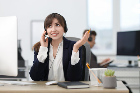 Saleswoman talking to client via headset at desk in officeの写真素材