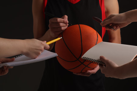 Sportsman signing autograph on basketball ball against black background, closeupの写真素材