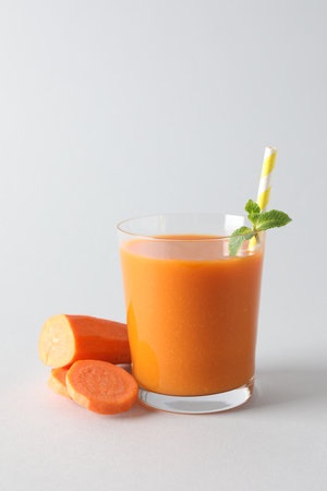 Fresh carrot smoothie in glass and cut vegetable on light grey backgroundの写真素材