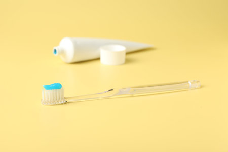 Toothbrush with toothpaste and tube on yellow background