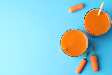 Fresh carrot smoothie in glasses and vegetables on light blue background, flat lay. Space for textの写真素材