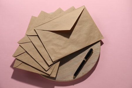 Kraft paper envelopes and pen on pink background, flat lay. Mockup for designの写真素材