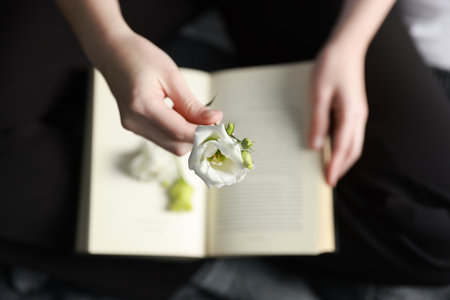 Woman holding beautiful flower bud above book on blanket, top viewの写真素材